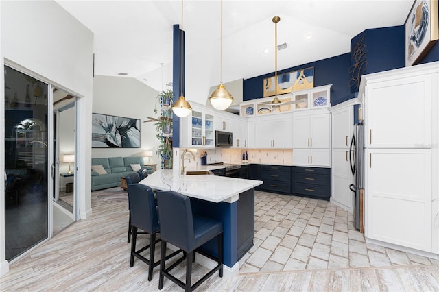 kitchen with tasteful backsplash, stainless steel appliances, decorative light fixtures, white cabinetry, and a breakfast bar area