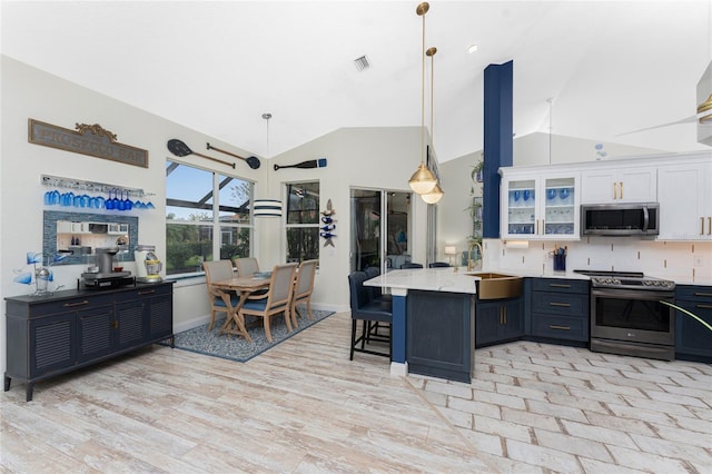 kitchen with hanging light fixtures, stainless steel appliances, backsplash, a kitchen bar, and white cabinets