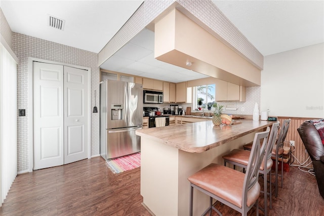 kitchen with a breakfast bar, dark hardwood / wood-style flooring, kitchen peninsula, stainless steel appliances, and cream cabinets