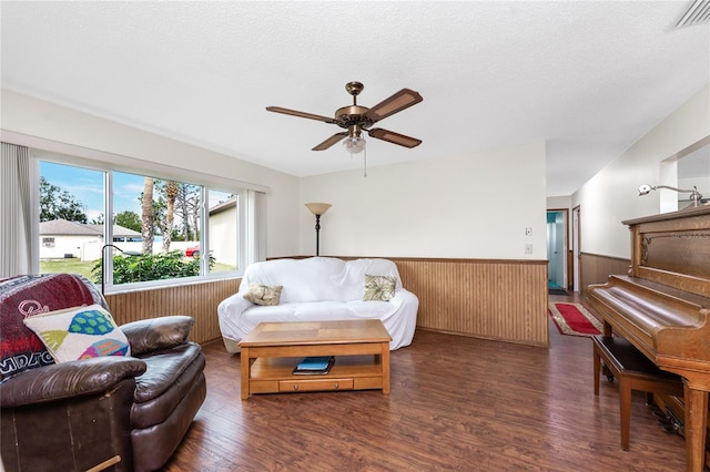 living area with ceiling fan, dark hardwood / wood-style flooring, a textured ceiling, and wood walls