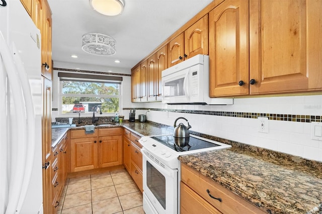 kitchen with light tile patterned floors, decorative backsplash, white appliances, dark stone counters, and sink