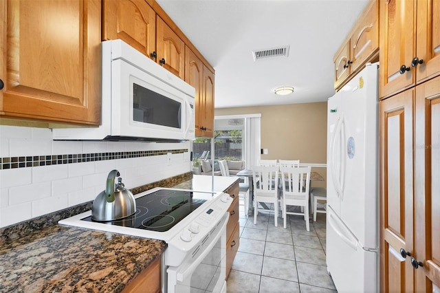 kitchen featuring light tile patterned floors, decorative backsplash, dark stone counters, and white appliances