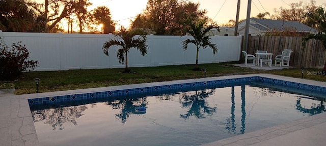 pool at dusk featuring a lawn and a patio area