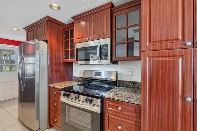 kitchen featuring appliances with stainless steel finishes, a textured ceiling, light tile patterned floors, and dark stone countertops