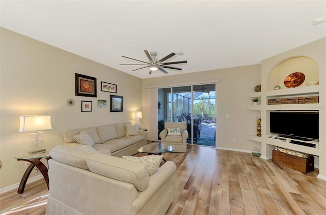 living room with built in shelves, ceiling fan, and light hardwood / wood-style flooring