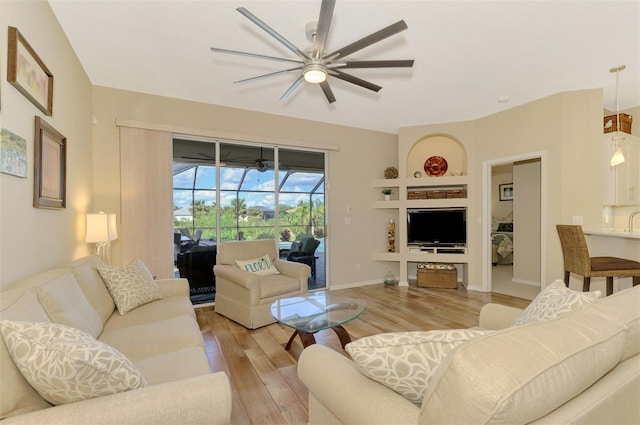 living room featuring built in shelves, hardwood / wood-style flooring, and ceiling fan