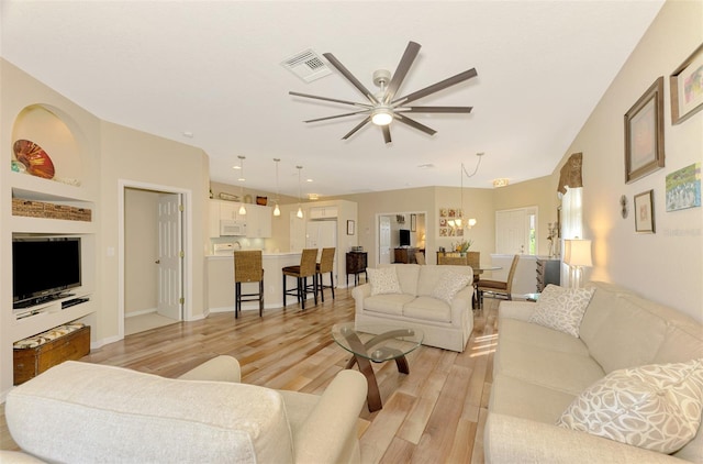 living room with ceiling fan with notable chandelier and light hardwood / wood-style flooring