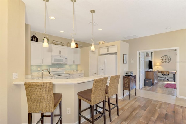 kitchen with kitchen peninsula, white appliances, pendant lighting, white cabinets, and hardwood / wood-style floors