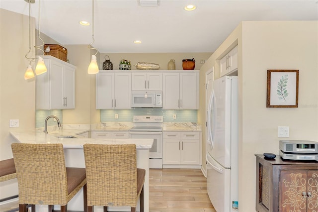 kitchen with white cabinetry, sink, kitchen peninsula, decorative light fixtures, and white appliances