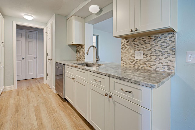 kitchen with decorative backsplash, white cabinetry, stainless steel dishwasher, and sink