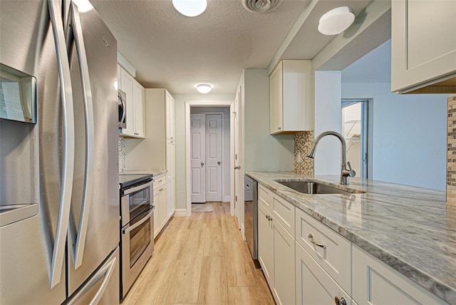 kitchen featuring light stone countertops, appliances with stainless steel finishes, sink, light hardwood / wood-style floors, and white cabinetry