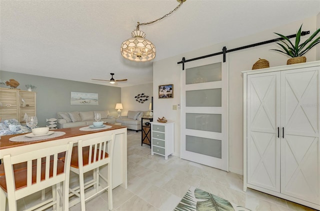 dining space featuring a barn door, ceiling fan, and a textured ceiling