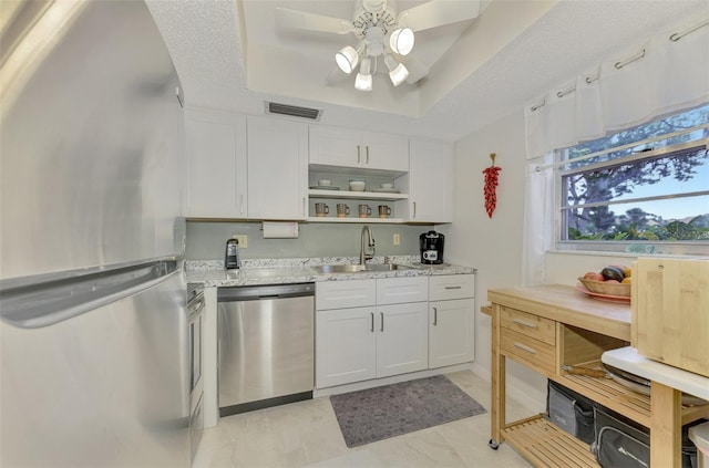 kitchen with light stone countertops, sink, a tray ceiling, white cabinets, and appliances with stainless steel finishes