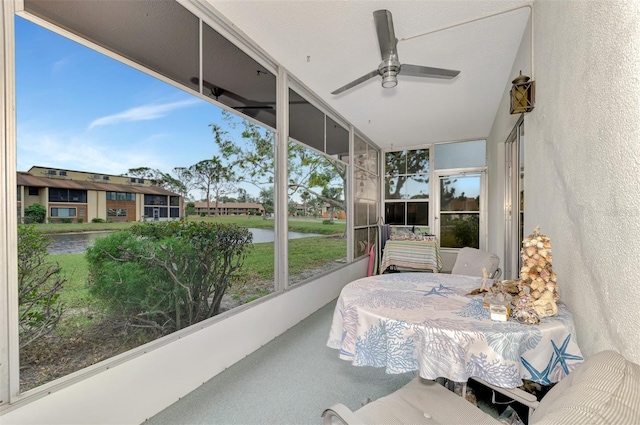 sunroom with ceiling fan and a water view