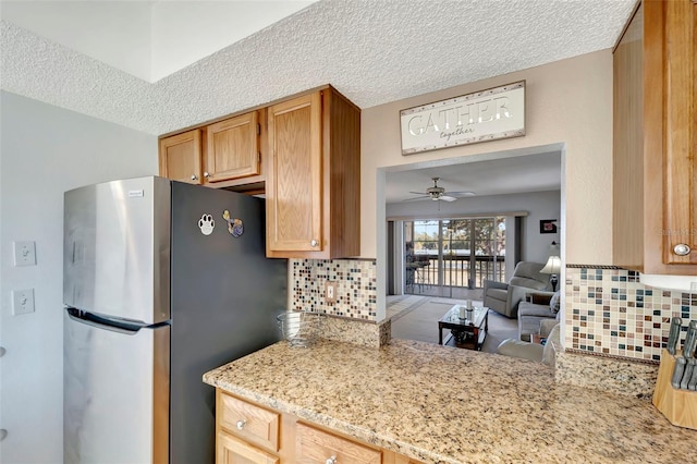 kitchen with a textured ceiling, backsplash, stainless steel refrigerator, and ceiling fan