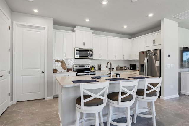 kitchen featuring sink, stainless steel appliances, a kitchen island with sink, a breakfast bar, and white cabinets