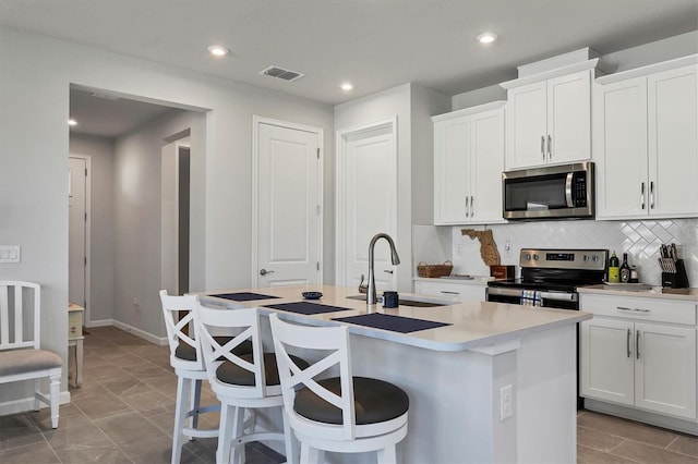 kitchen featuring white cabinets, sink, an island with sink, appliances with stainless steel finishes, and tasteful backsplash