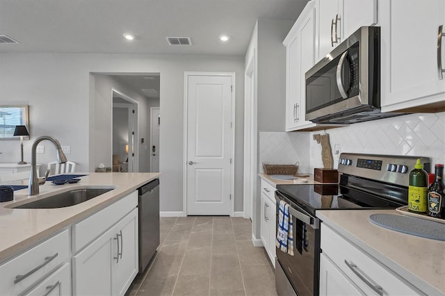 kitchen featuring sink, stainless steel appliances, light tile patterned floors, tasteful backsplash, and white cabinets