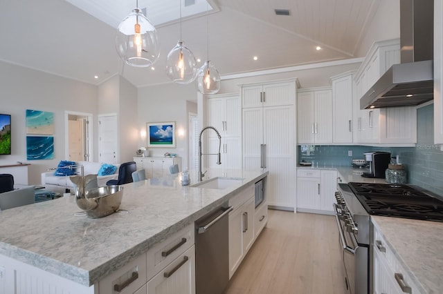 kitchen featuring sink, white cabinets, wall chimney exhaust hood, a kitchen island with sink, and appliances with stainless steel finishes