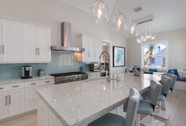 kitchen featuring white cabinets, a kitchen island with sink, wall chimney exhaust hood, and decorative backsplash