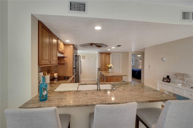 kitchen with stainless steel refrigerator, kitchen peninsula, a textured ceiling, a breakfast bar, and sink