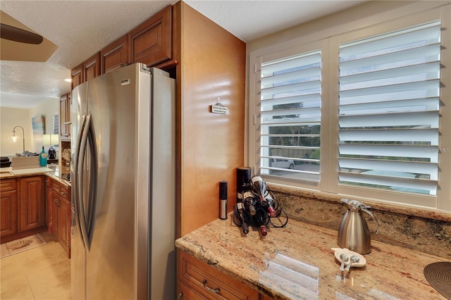 kitchen with a textured ceiling, light tile patterned floors, light stone counters, and stainless steel fridge