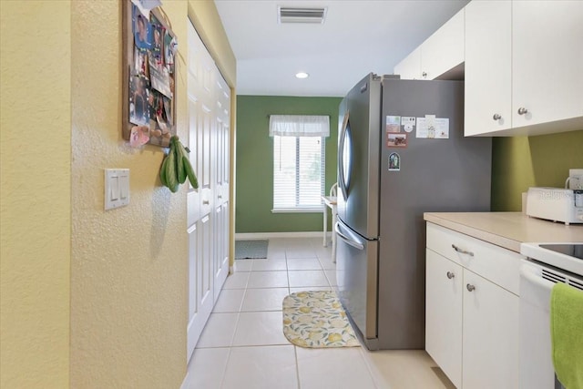 kitchen featuring white range with electric stovetop, light tile patterned floors, stainless steel fridge, and white cabinets