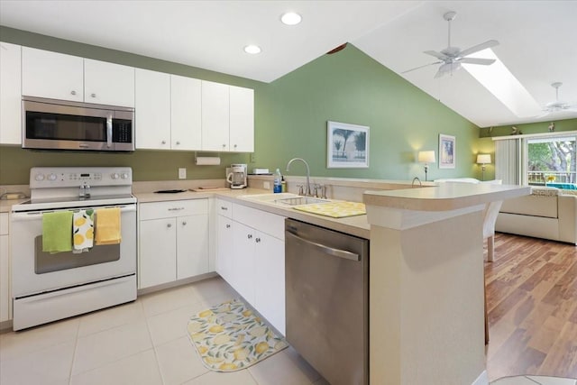 kitchen with lofted ceiling with skylight, appliances with stainless steel finishes, white cabinets, and kitchen peninsula