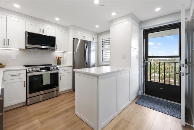 kitchen featuring white cabinetry, stainless steel appliances, backsplash, kitchen peninsula, and light wood-type flooring