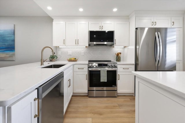 kitchen with decorative backsplash, sink, light wood-type flooring, appliances with stainless steel finishes, and white cabinets