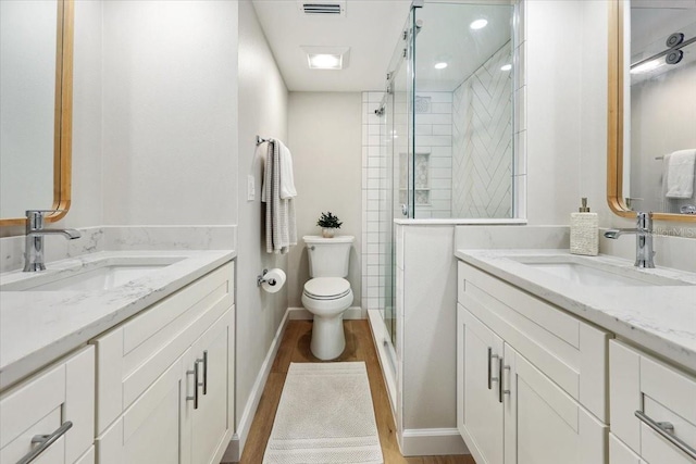 bathroom with hardwood / wood-style flooring, toilet, vanity, and a shower with door