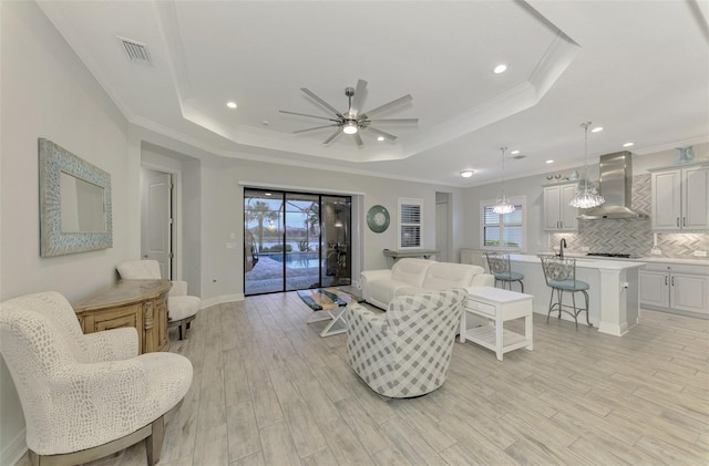 living room with ceiling fan, light hardwood / wood-style floors, and a tray ceiling