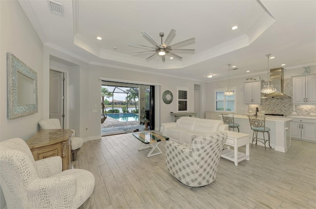 living room with ceiling fan, crown molding, a raised ceiling, and light wood-type flooring