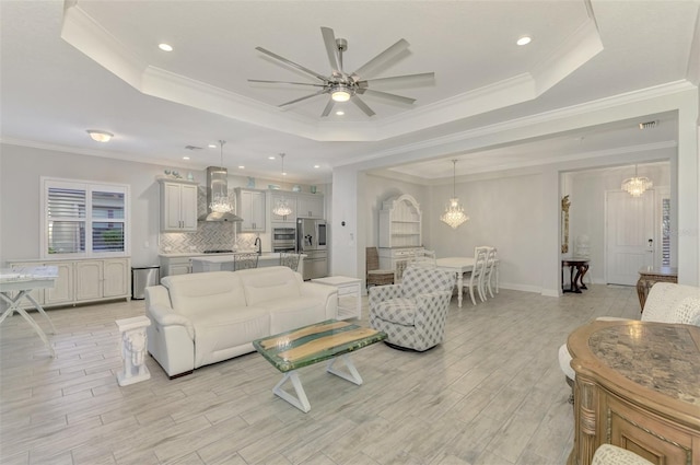 living room featuring ceiling fan with notable chandelier, a tray ceiling, and crown molding