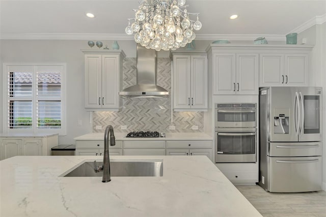 kitchen featuring appliances with stainless steel finishes, decorative light fixtures, light stone countertops, wall chimney exhaust hood, and sink