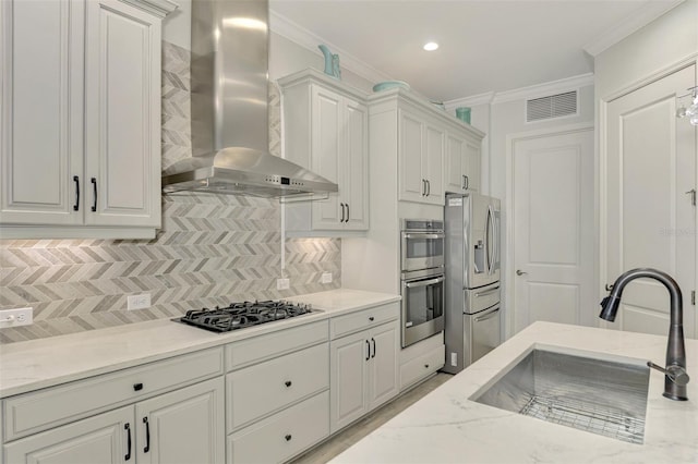 kitchen featuring stainless steel appliances, backsplash, wall chimney range hood, white cabinets, and sink