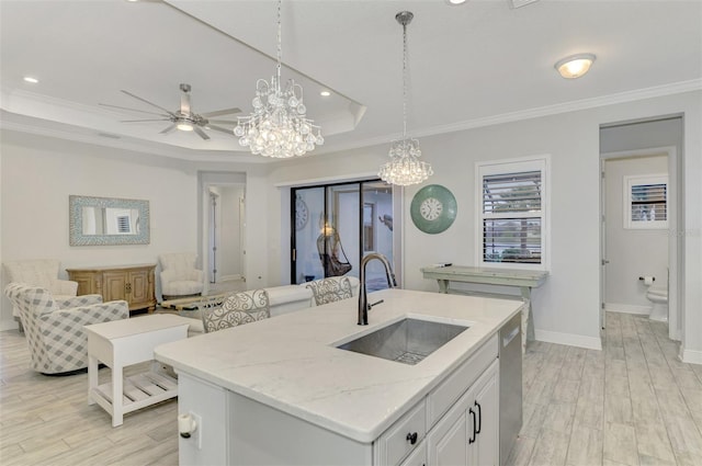 kitchen featuring a center island with sink, a raised ceiling, sink, crown molding, and white cabinetry