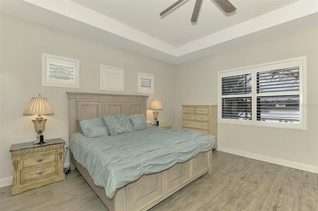 bedroom with ceiling fan, a raised ceiling, and light hardwood / wood-style flooring