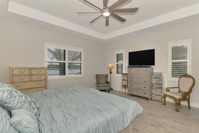 bedroom with ceiling fan, a tray ceiling, and light wood-type flooring