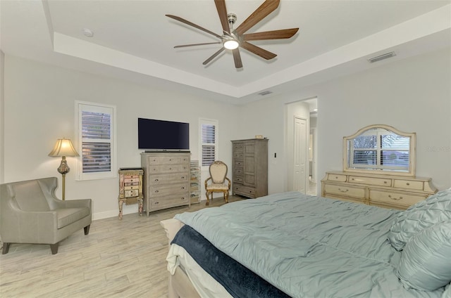 bedroom with ceiling fan, a tray ceiling, and light hardwood / wood-style floors