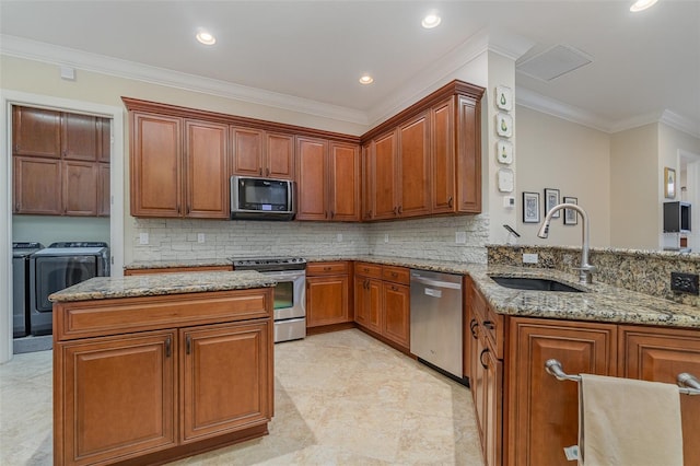 kitchen featuring appliances with stainless steel finishes, independent washer and dryer, light stone countertops, ornamental molding, and sink