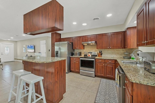 kitchen featuring light stone countertops, appliances with stainless steel finishes, sink, light tile patterned floors, and a breakfast bar area