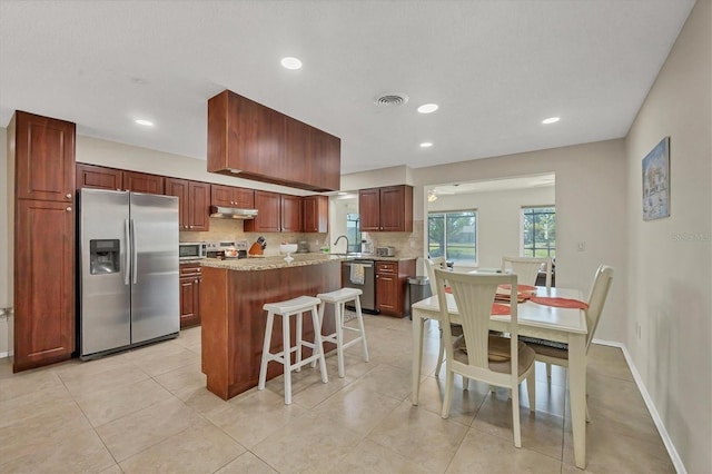 kitchen with decorative backsplash, light stone counters, light tile patterned flooring, a kitchen bar, and stainless steel appliances