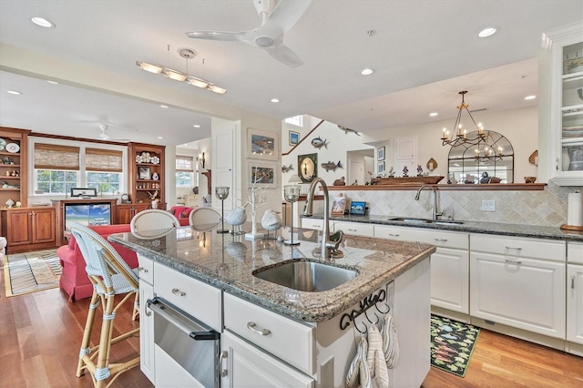 kitchen with decorative light fixtures, sink, white cabinetry, and a kitchen island with sink