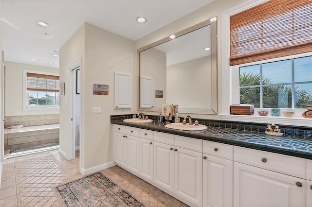 bathroom featuring tile patterned flooring, a relaxing tiled tub, and vanity