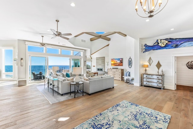 living room with ceiling fan with notable chandelier, light hardwood / wood-style flooring, and a high ceiling