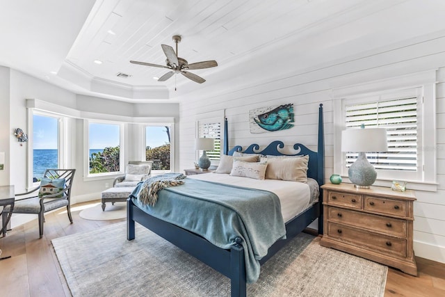 bedroom featuring crown molding, ceiling fan, a water view, wood-type flooring, and a raised ceiling