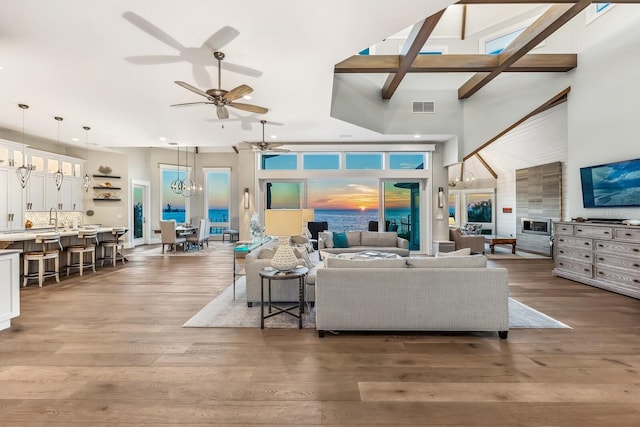 living room featuring ceiling fan with notable chandelier, sink, hardwood / wood-style floors, and a high ceiling