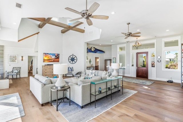 living room with a towering ceiling, ceiling fan with notable chandelier, and light wood-type flooring