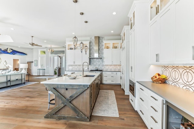 kitchen with wine cooler, sink, white cabinetry, a center island with sink, and pendant lighting